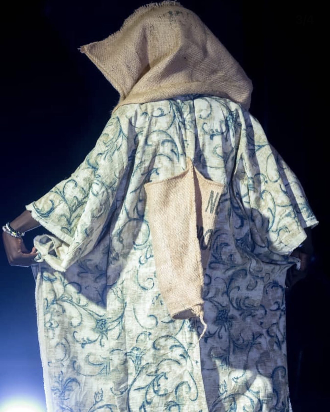 Model wearing printed sisal kaftan robe with hooded sisal headwrap on a night stage — dramatic stage lighting