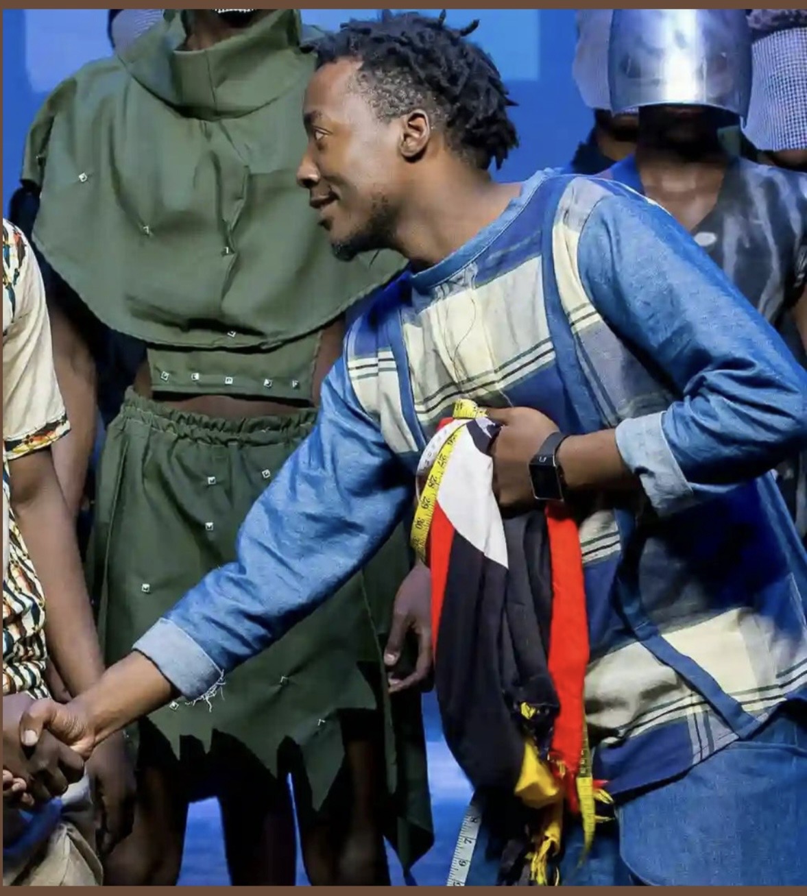 Mukasa Najib backstage at a fashion show — holding a tape measure and fabric, working with models during a Bobbin Case runway production