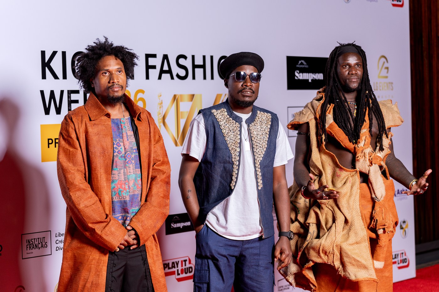Mukasa Najib flanked by collaborators wearing Bobbin Case gunia and African textile looks on the Kigali Fashion Week 2026 red carpet