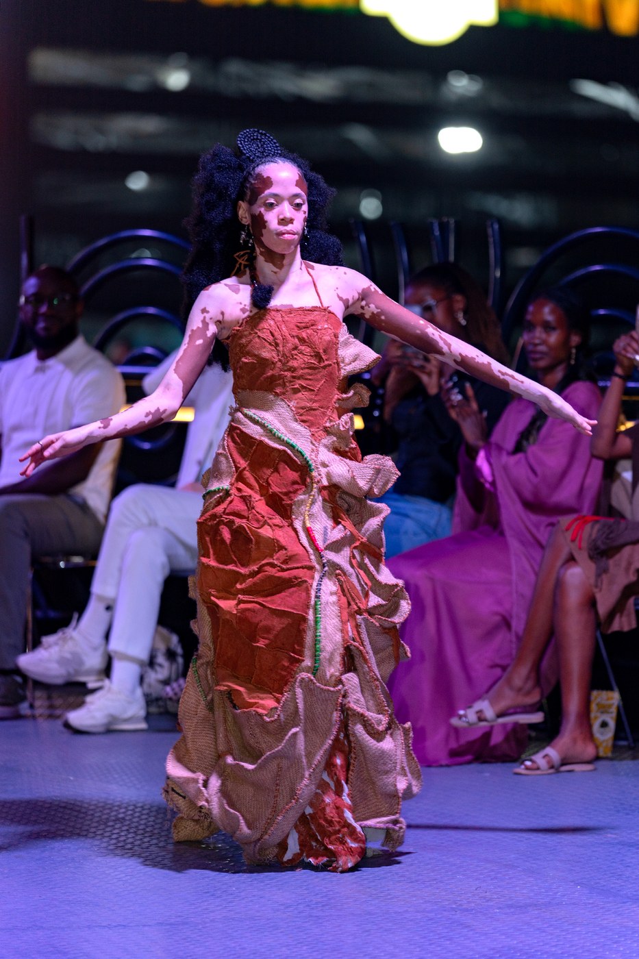 Model arms outstretched in layered gunia sack gown on the Bobbin Case runway at Kigali Fashion Week 2026 — full length